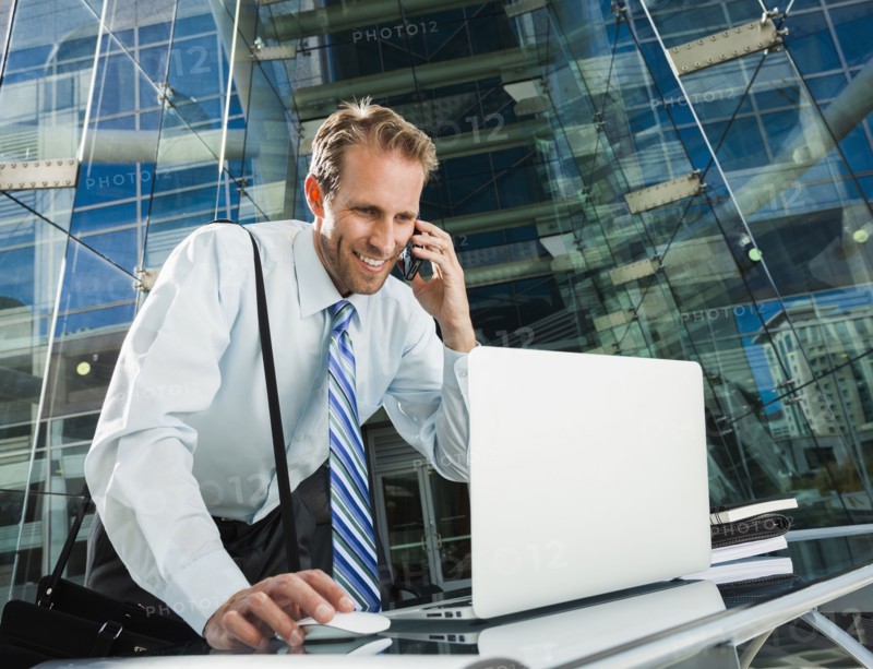 Caucasian businessman talking on cell phone at laptop