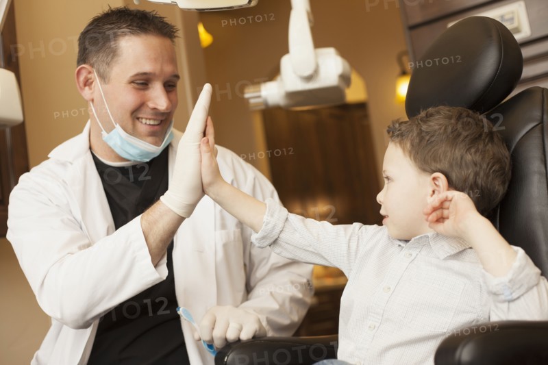 Caucasian dentist and boy high fiving in office