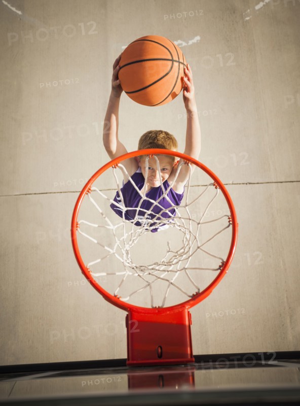 Caucasian boy dunking basketball in hoop