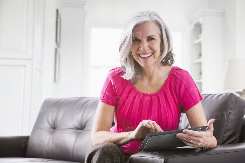 Portrait of smiling Caucasian woman using digital tablet on sofa