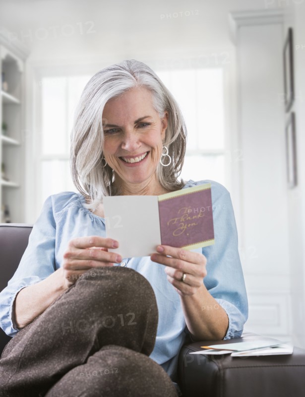 Happy Caucasian woman reading card on sofa