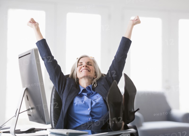 Happy Caucasian businesswoman with feet up on desk