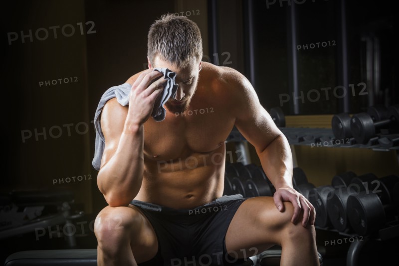 Tired Caucasian man wiping sweat off forehead in gym