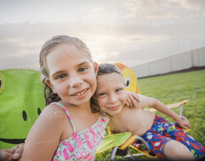 Caucasian children relaxing in lawn chairs in backyard