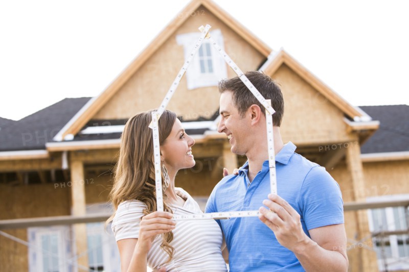 Caucasian couple holding frame near house under construction