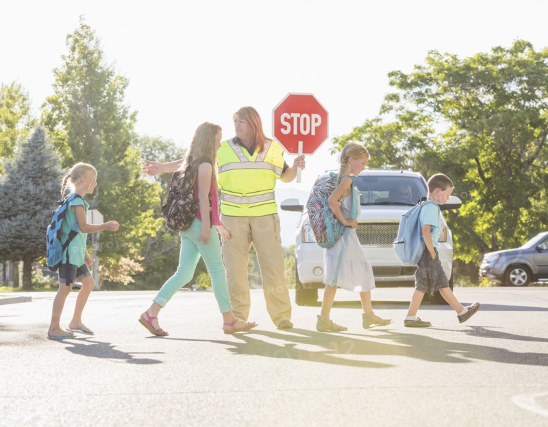 Caucasian crossing guard helping children in crosswalk