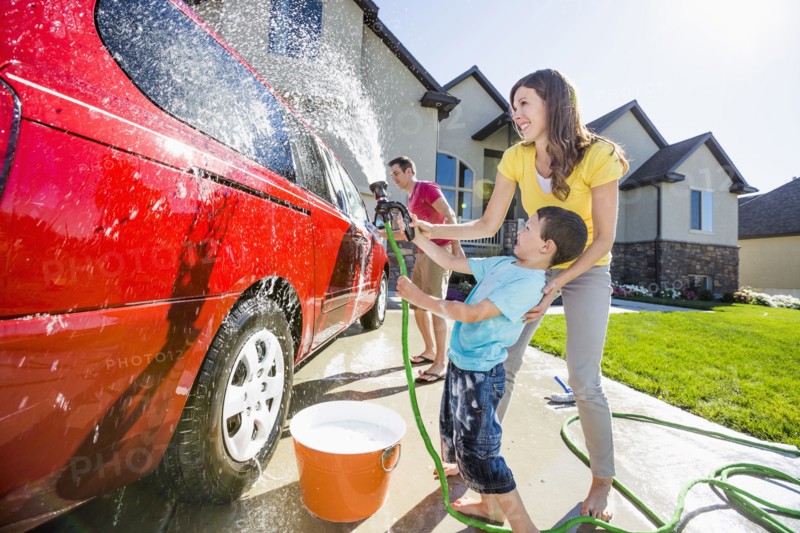 Caucasian family spraying water on car in driveway