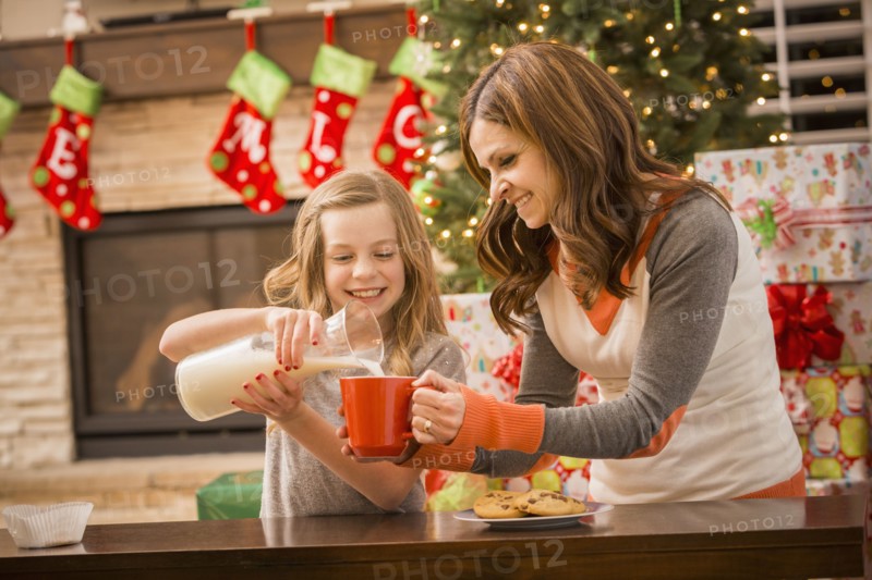Caucasian mother and daughter leaving cookies and milk for Santa at Christmas