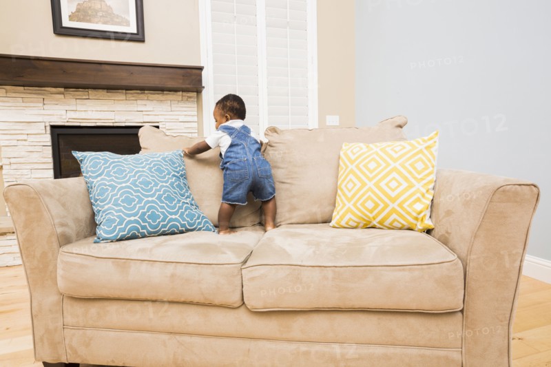 Black baby climbing on sofa in living room