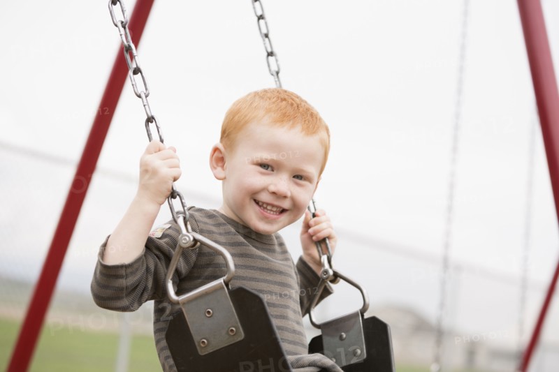 Caucasian boy sitting on playground swing