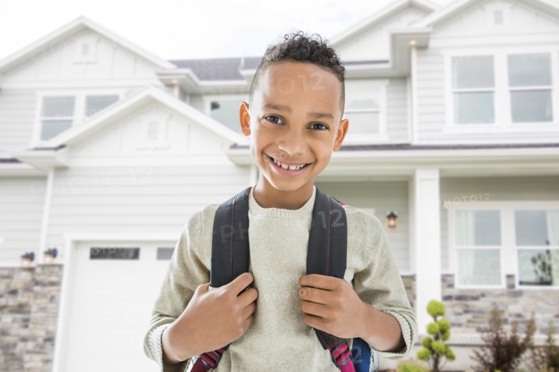 Black boy in backpack smiling outside house