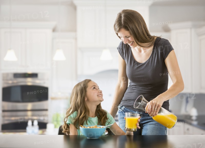Caucasian mother pouring juice for daughter in kitchen