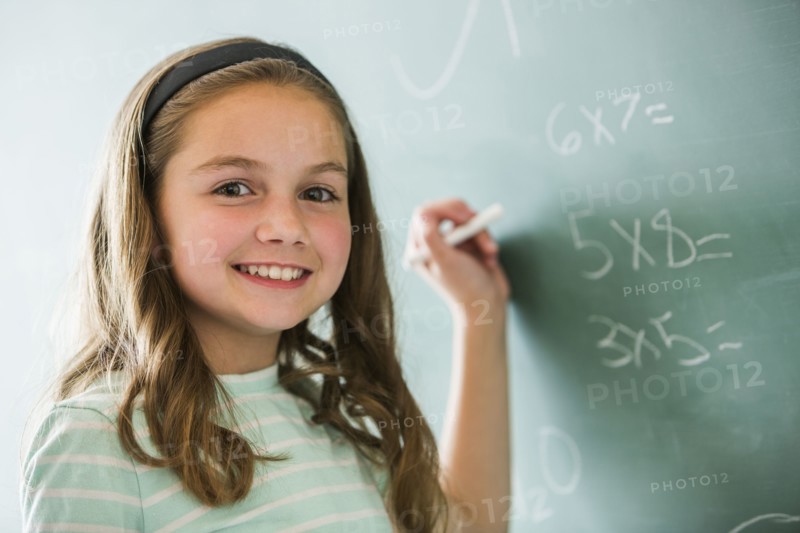 Caucasian girl doing math problems on chalkboard
