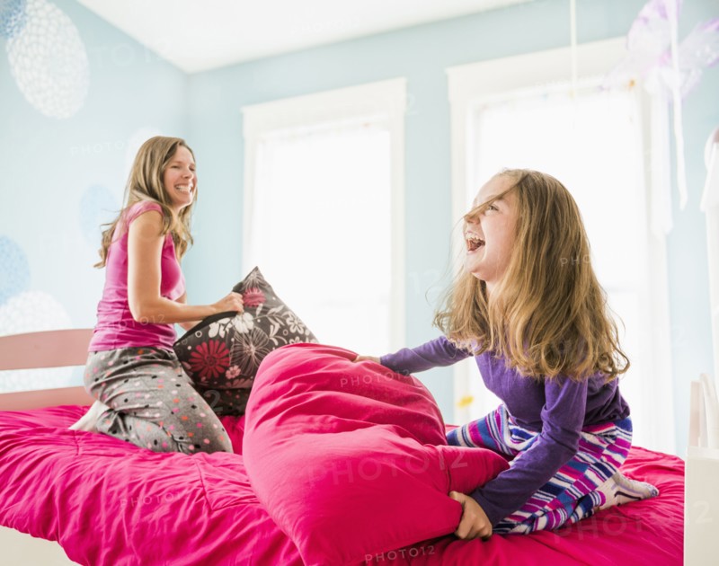 Caucasian mother and daughter having pillow fight on bed