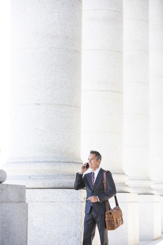Mixed race businessman talking on cell phone under columns