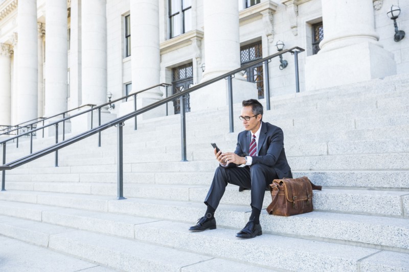 Mixed race businessman using cell phone on courthouse steps