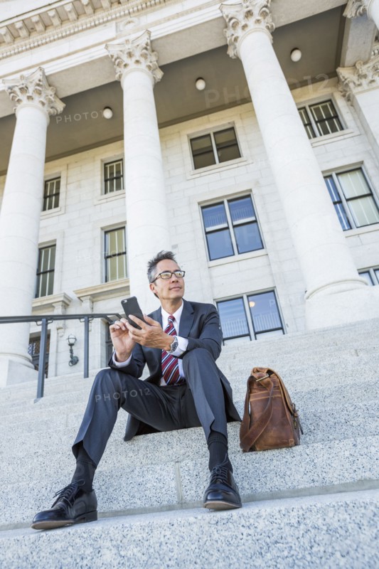 Mixed race businessman using cell phone on courthouse steps