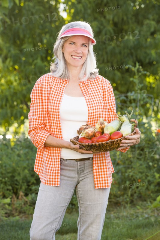 Caucasian woman holding basket of vegetables in garden