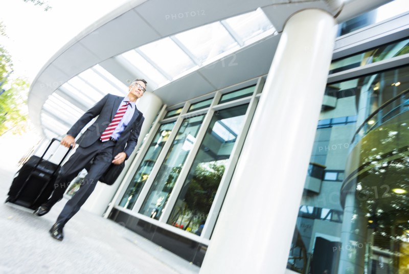 Mixed race businessman rolling luggage in office
