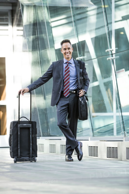 Mixed race businessman rolling luggage outdoors