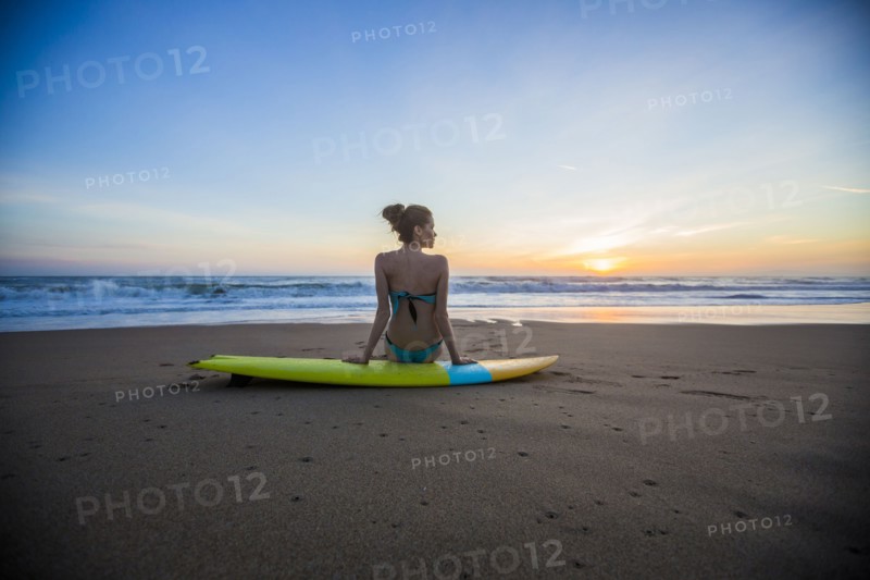 Caucasian woman sitting on surfboard on beach