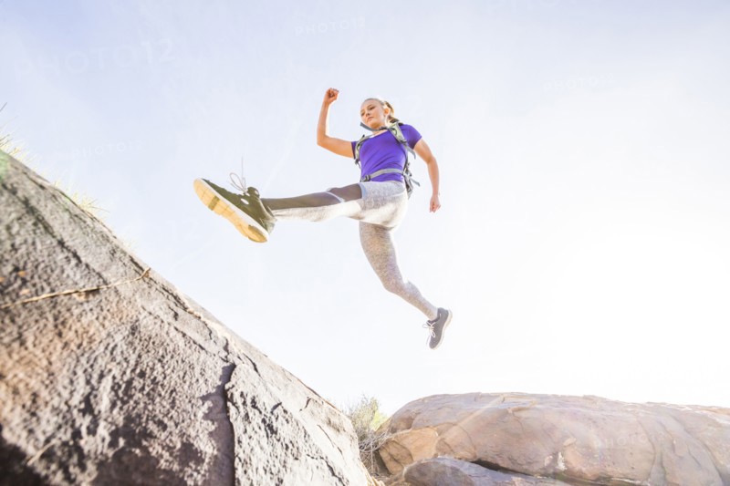 Caucasian woman leaping over boulders