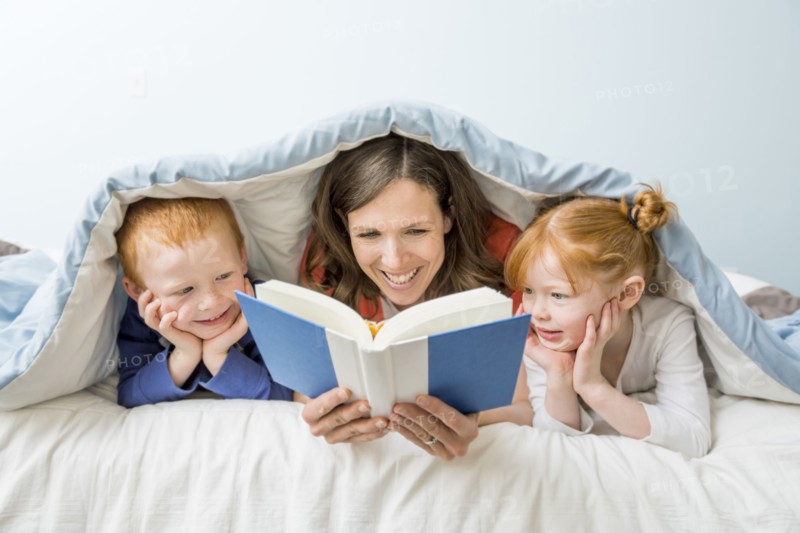 Caucasian mother and children reading book in bed