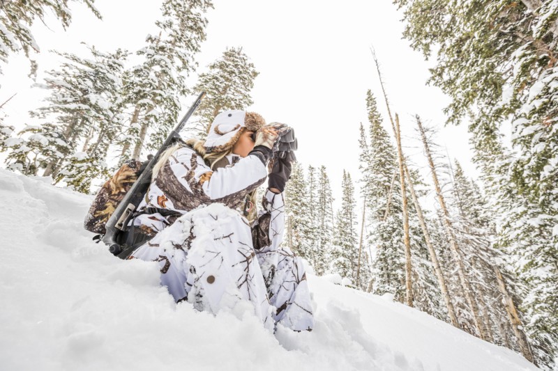 Caucasian woman hunting in forest using binoculars