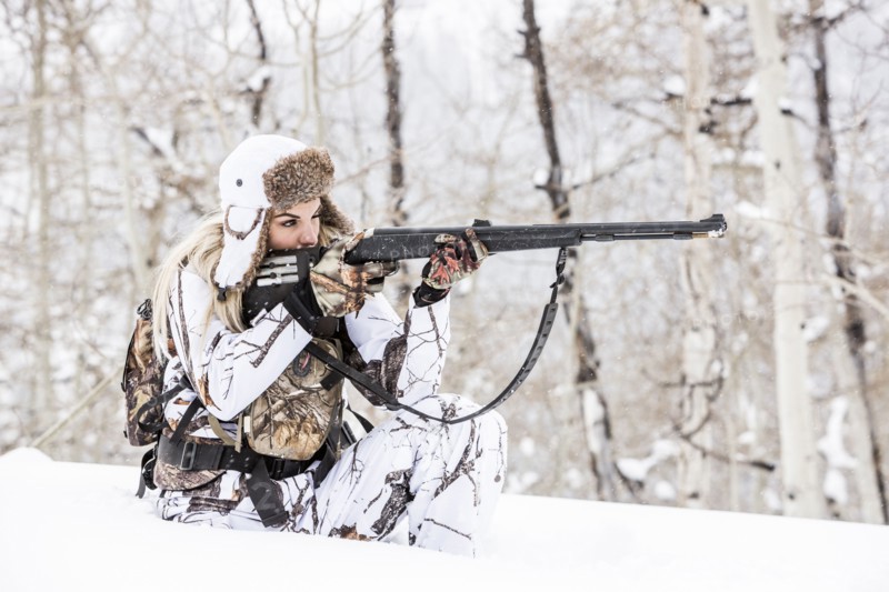 Caucasian woman hunting in forest aiming rifle