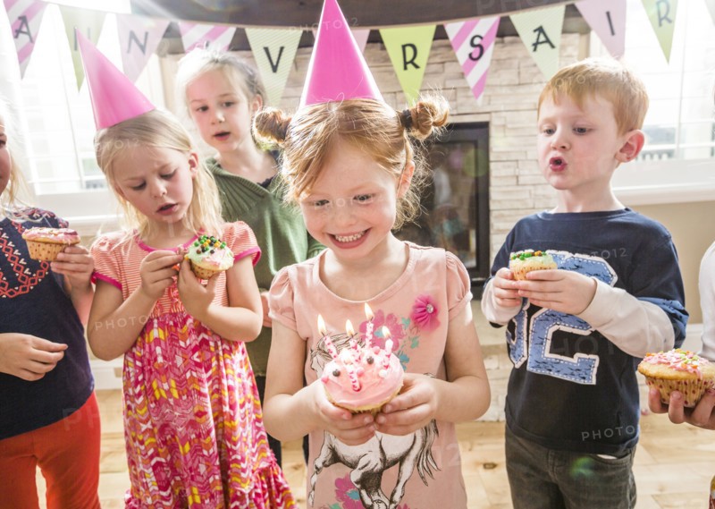 Caucasian girl wearing party hat holding cupcake with burning candles