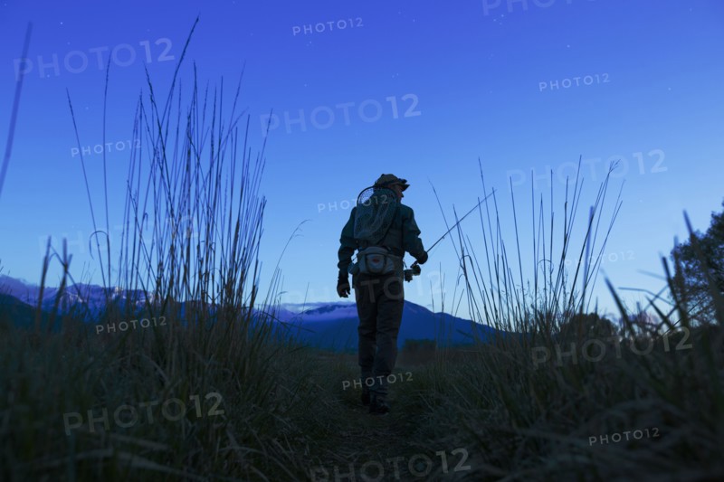 Caucasian man carrying fishing rod in field at dawn