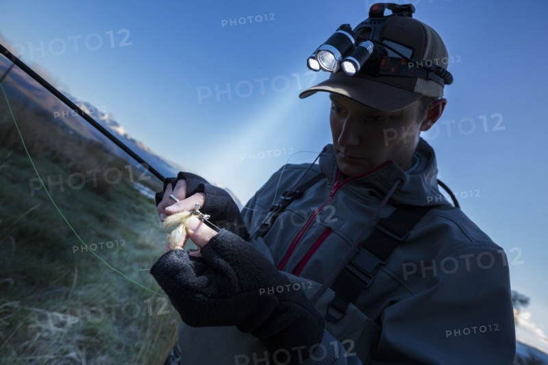 Caucasian man wearing headlamp baiting hook at dawn
