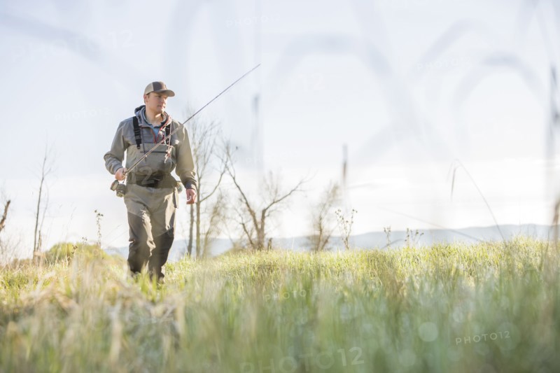 Caucasian man carrying fishing rod in field
