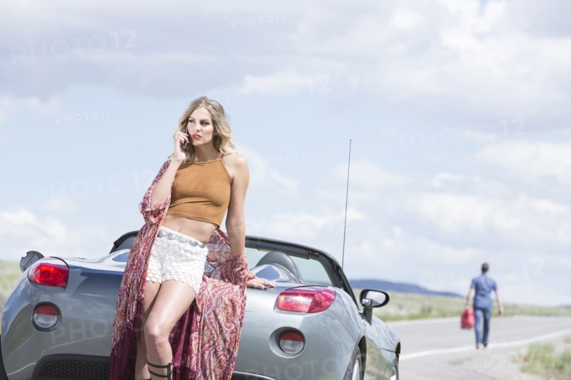 Caucasian woman talking on cell phone at vehicle breakdown