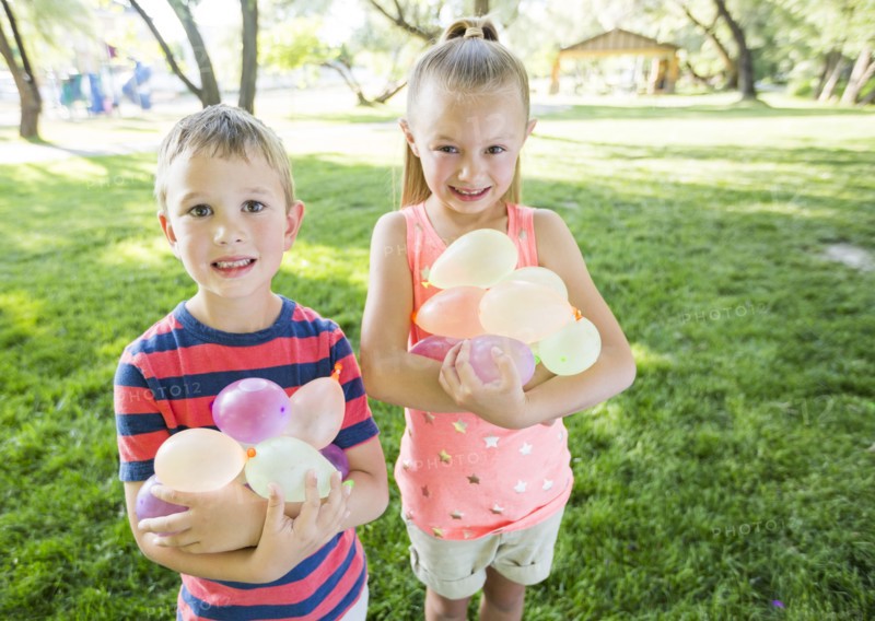 Caucasian brother and sister holding water balloons