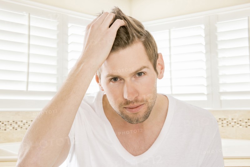 Serious Caucasian man styling hair in bathroom