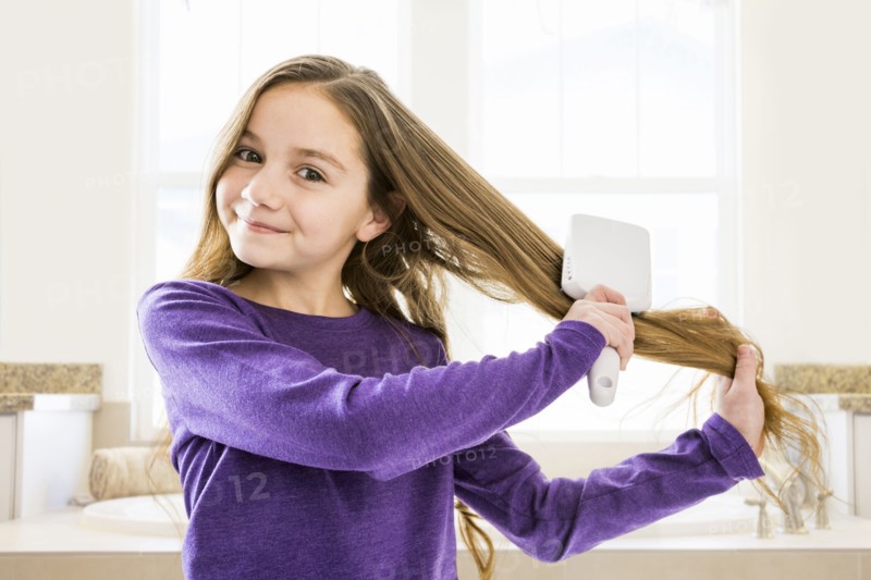 Caucasian girl brushing hair in bathroom