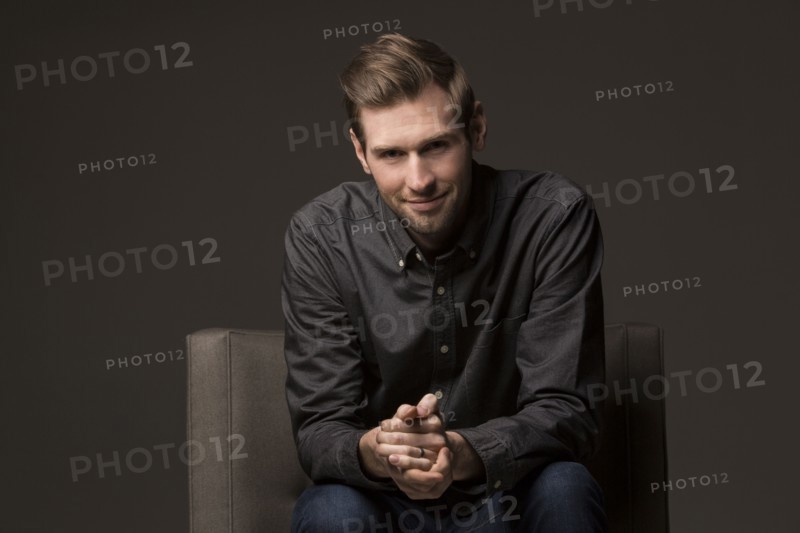 Smiling Caucasian man with hands clasped in armchair