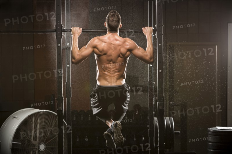 Caucasian man doing chin-up in gymnasium
