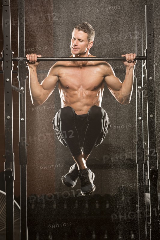 Caucasian man doing chin-up in gymnasium