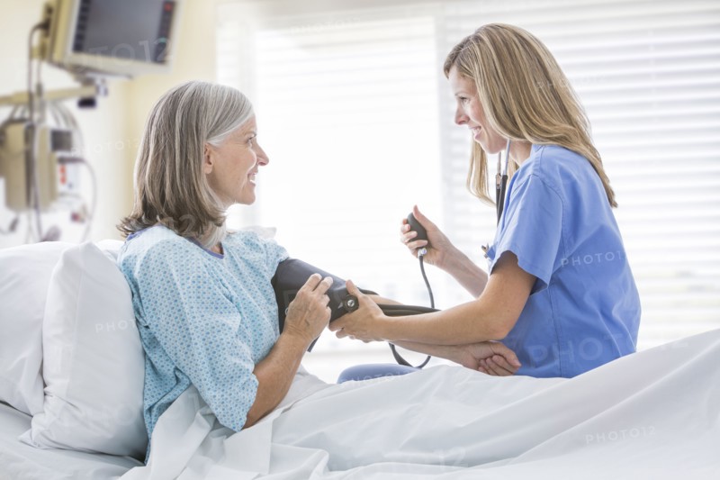 Caucasian nurse measuring blood pressure of woman in hospital bed