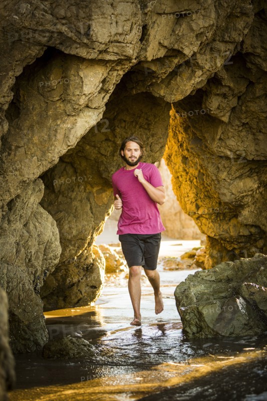 Caucasian man running under rock formation at beach