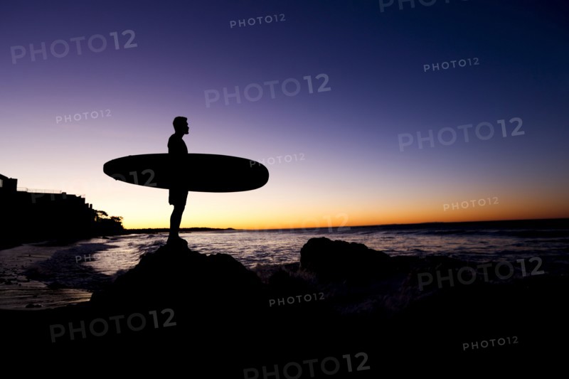 Silhouette of Hispanic man holding surfboard at beach