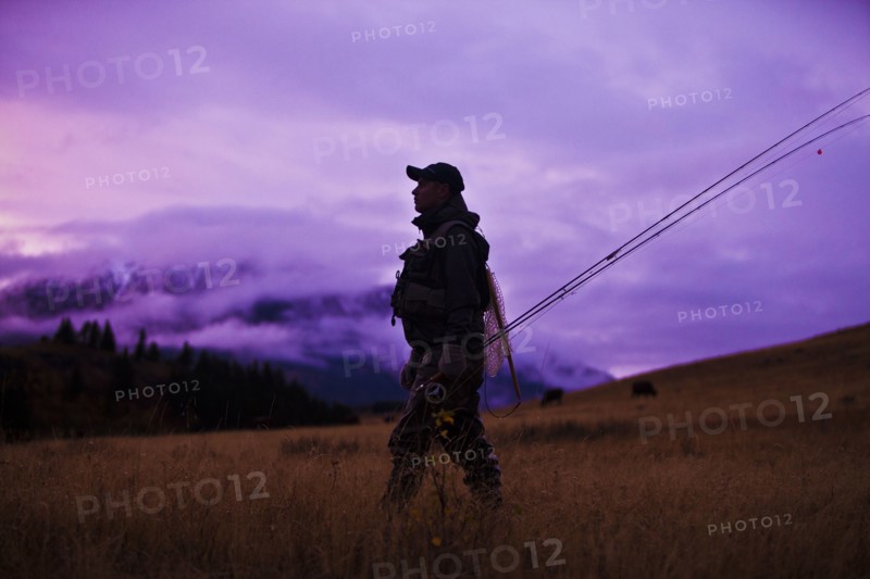 Caucasian man walking and carrying fishing rods