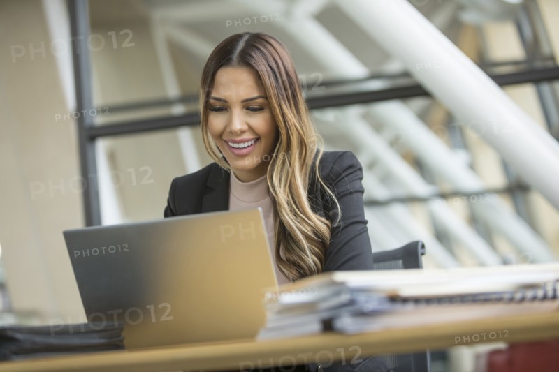 Smiling Mixed Race businesswoman using laptop