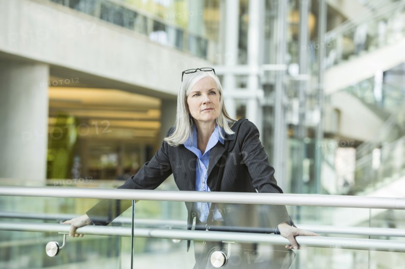 Portrait of serious Caucasian businesswoman leaning on railing in lobby