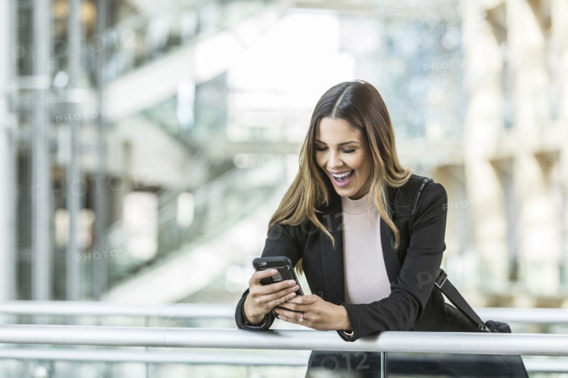Mixed Race businesswoman texting on cell phone leaning on railing in lobby