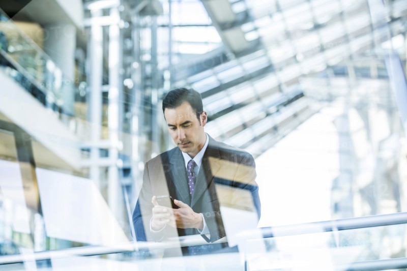 Mixed Race businessman texting on cell phone leaning on railing in lobby