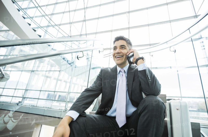 Smiling Mixed Race businessman sitting on staircase talking on cell phone