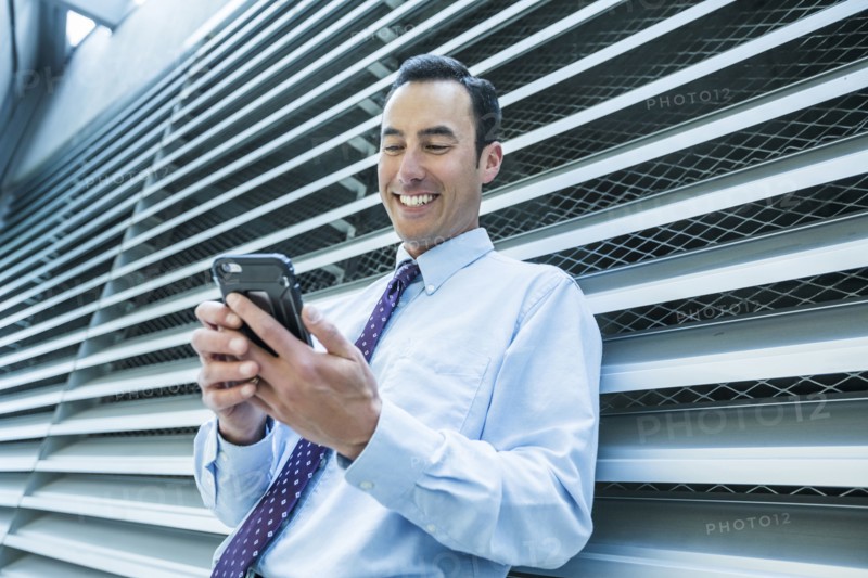 Smiling Mixed Race businessman leaning on wall texting on cell phone